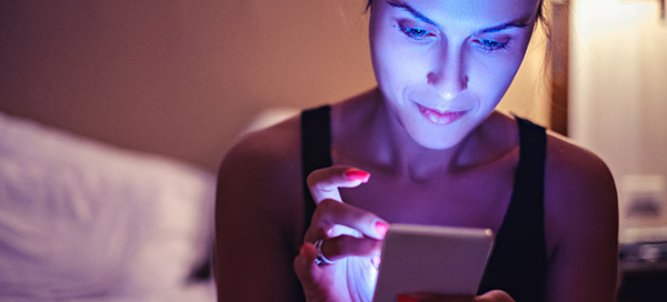Woman scrolls through phone at bedtime, face bathed in blue light