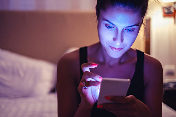 Woman scrolls through phone at bedtime, face bathed in blue light